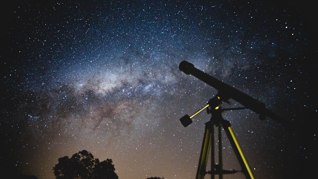 Silhouette of a telescope pointed at the Milky Way at night