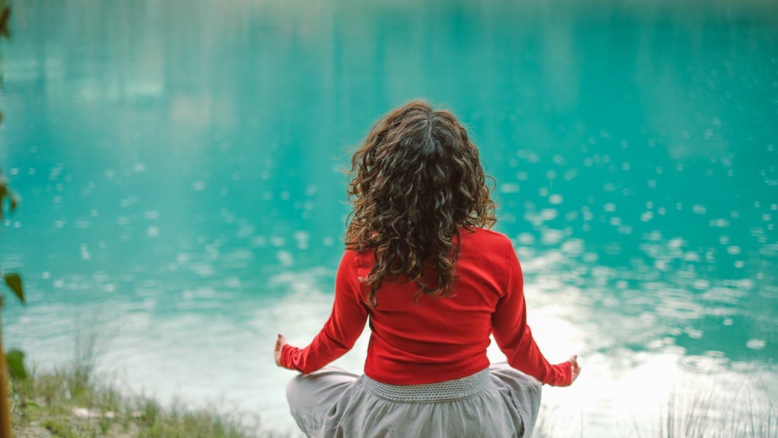 A woman meditating peacefully beside a calm lake